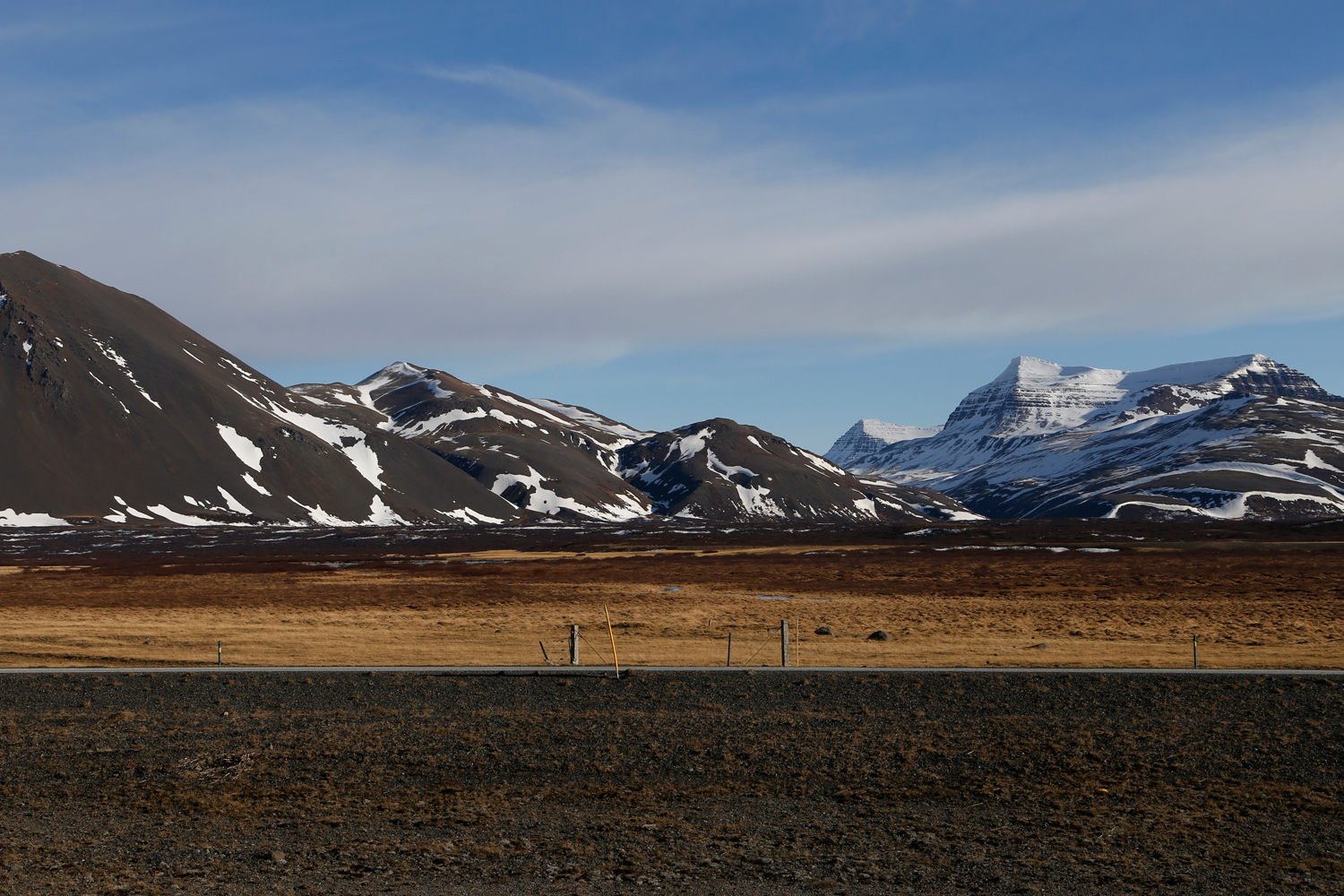 A deserted street runs in a straight horizontal line below snow-capped mountains glistening in the sunshine.